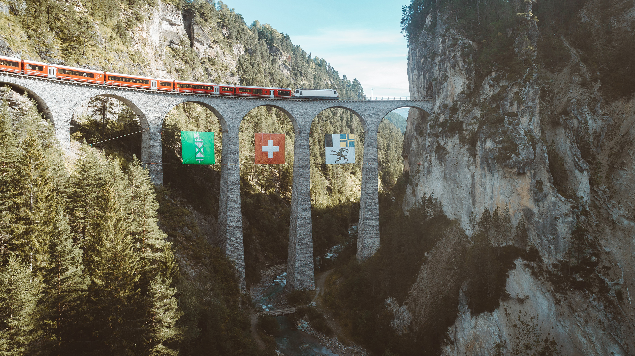 Brücke mit Zug und Flaggen der Kantone umgeben von Felsen